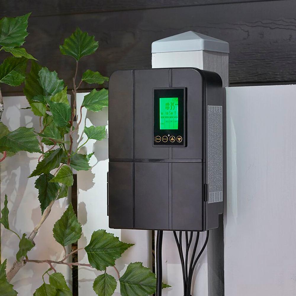 low voltage black transformer hung up on a white fence with leave around it